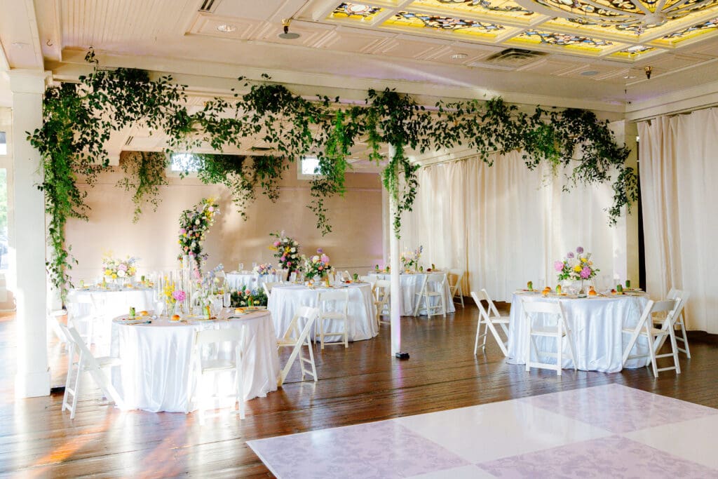Garden-inspired wedding reception design at Ant Street Inn in Brenham, Texas with suspended greenery, floral centerpieces, and custom dance floor.