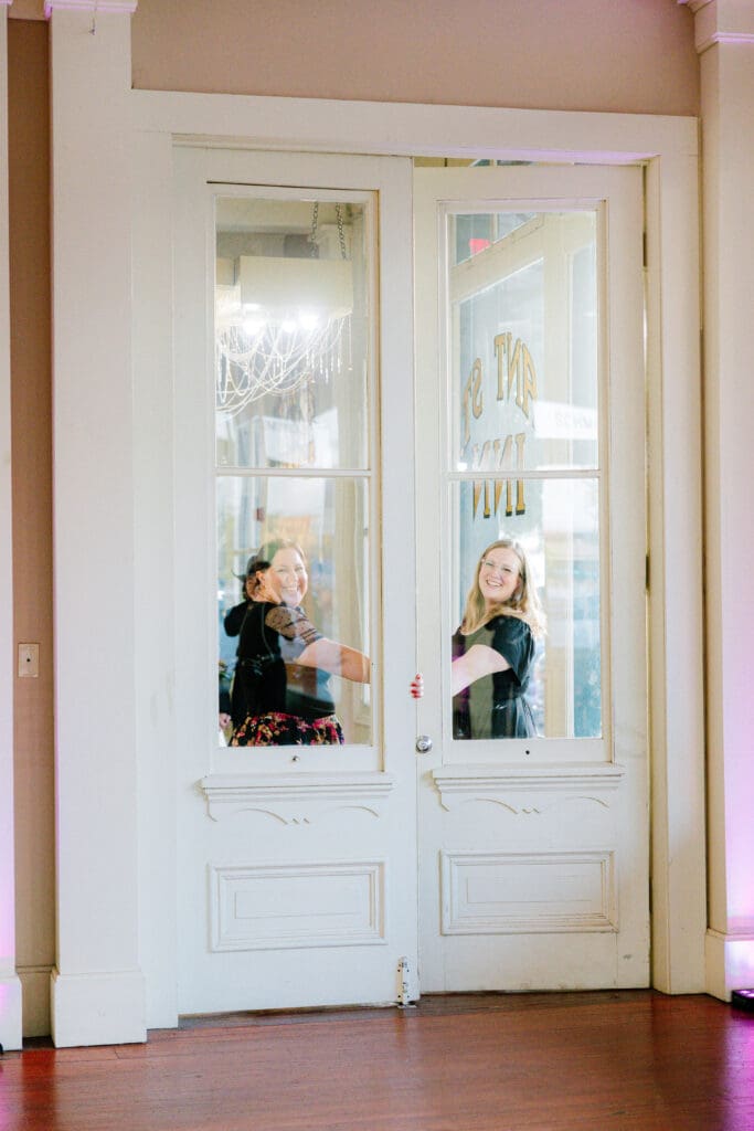 Wedding guests share a fun candid moment behind the vintage entry doors at Ant Street Inn in Brenham, Texas during Alexandra and Gage's wedding reception.