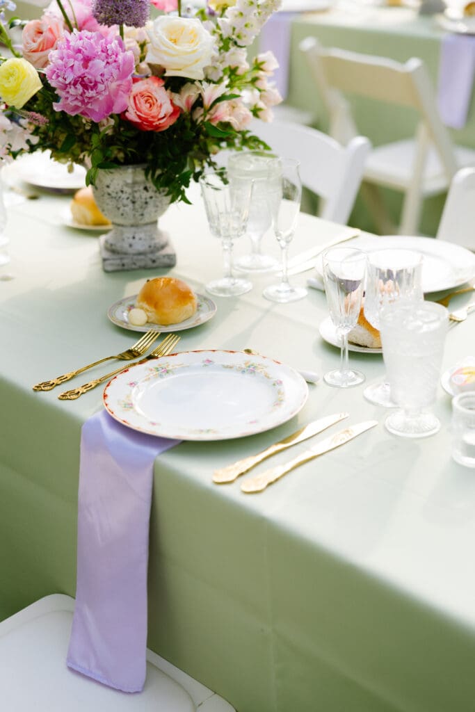 Garden-inspired wedding tablescape with vintage china, gold flatware, pastel florals, and sage green linens styled for an outdoor reception.