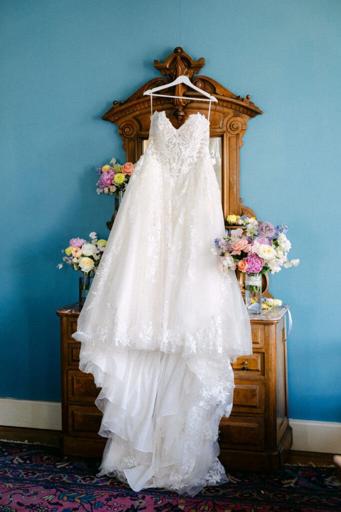 Bride's lace wedding dress displayed before the ceremony at Ant Street Inn in Brenham, Texas with colorful wedding florals.