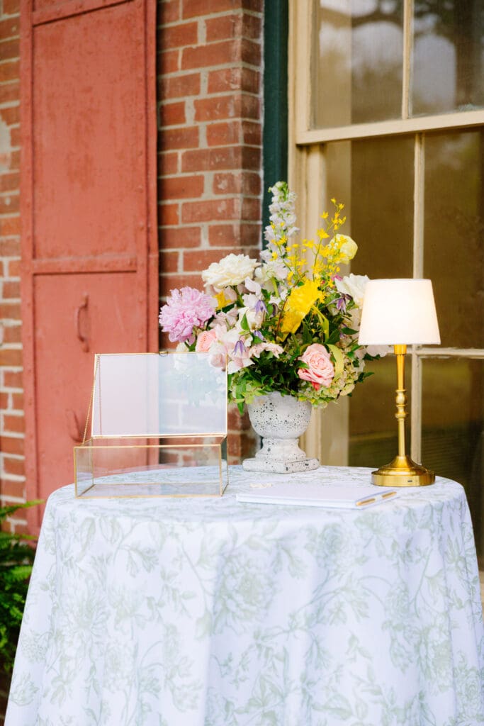 Guest book display at Alexandra and Gage's Ant Street Inn wedding in Brenham, Texas, featuring colorful garden-inspired florals, vintage-inspired décor, gold accents, and a floral-patterned linen.