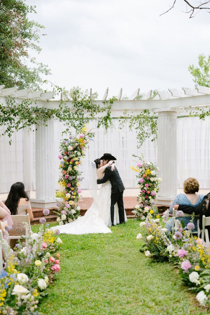 Bride and groom share their first kiss during an outdoor garden wedding ceremony at Ant Street Inn in Brenham, Texas.